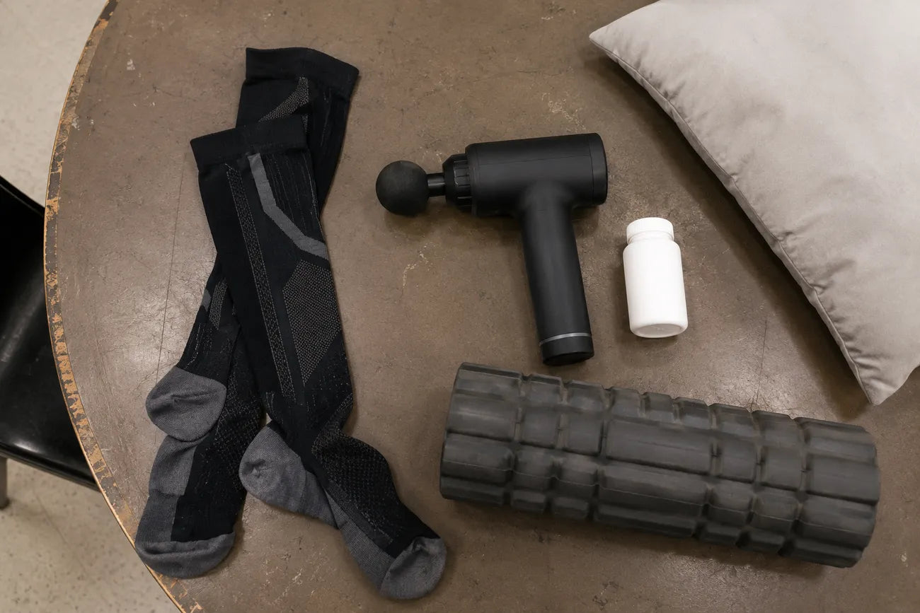Flat-lay of failed fixes: compression socks, massage gun, painkillers, foam roller, pillow